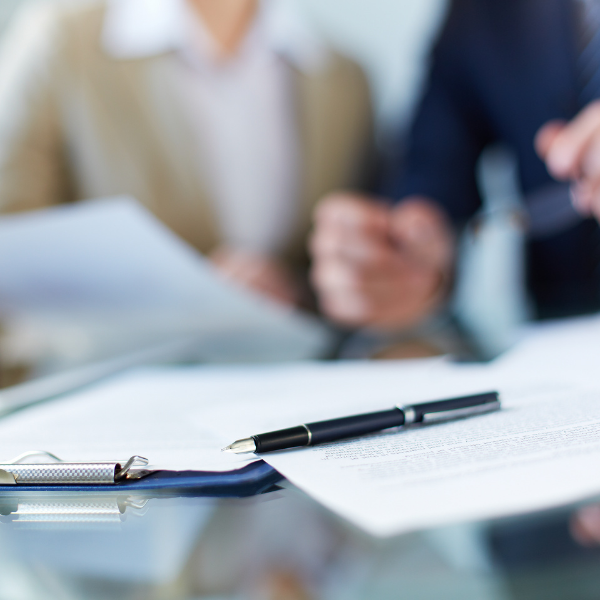 Files on the table with pen on top and two people in the background