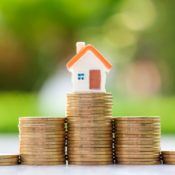 Small house figurine placed upon stacks of coins