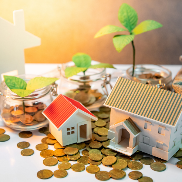 Small house figurines placed on top of scattered coins and plants